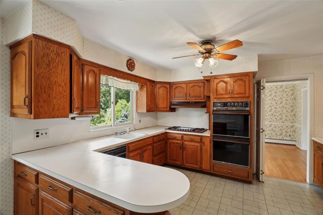 Kitchen featuring brown cabinets, wallpapered walls, dobule oven black, and a sink | Image 6