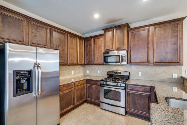 Kitchen with light tile floor, light stone counters, appliances with stainless steel finishes, and tasteful backsplash | Image 7