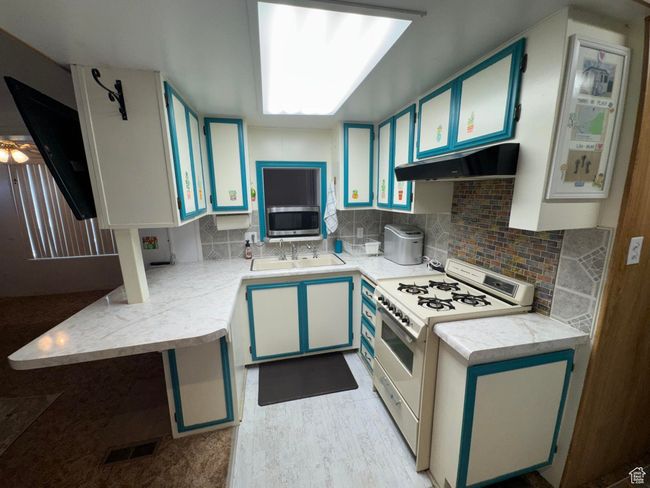 Kitchen with white range with gas cooktop, under cabinet range hood, light countertops, stainless steel microwave, and backsplash | Image 11