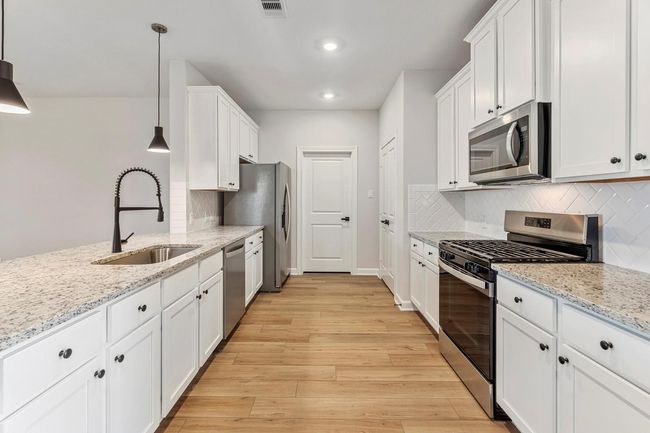 In this kitchen, white cabinets exude a sense of freshness and purity, perfectly paired with the luminous beauty of white granite countertops. The open layout fosters a welcoming atmosphere, inviting conversation and interaction between the kitchen and living area | Image 5