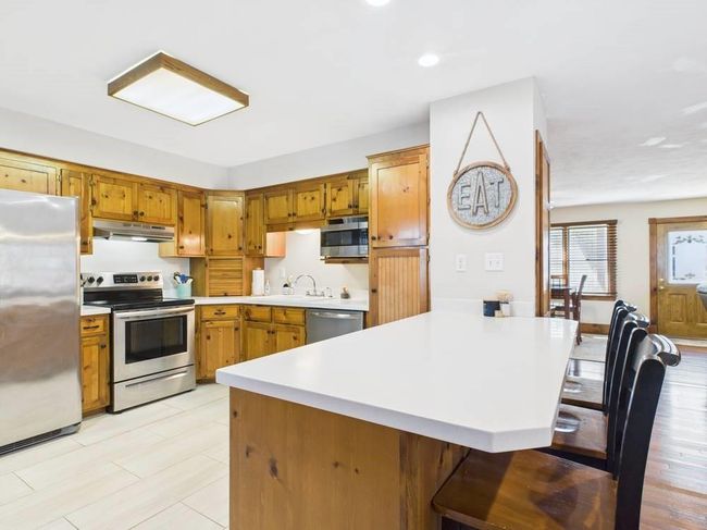 Kitchen featuring light countertops, appliances with stainless steel finishes, a kitchen bar, a peninsula, and under cabinet range hood | Image 36