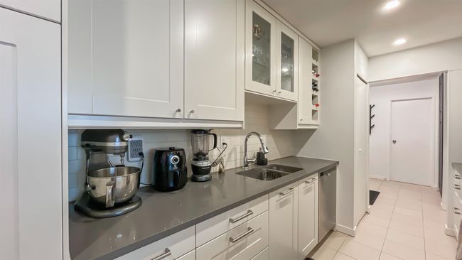 Kitchen featuring tasteful backsplash, light tile patterned floors, glass insert cabinets, dark countertops, and a sink | Image 5