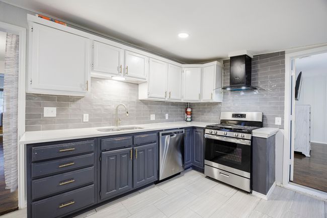 Kitchen with wall chimney range hood, light countertops, white cabinets, appliances with stainless steel finishes, and a sink | Image 11