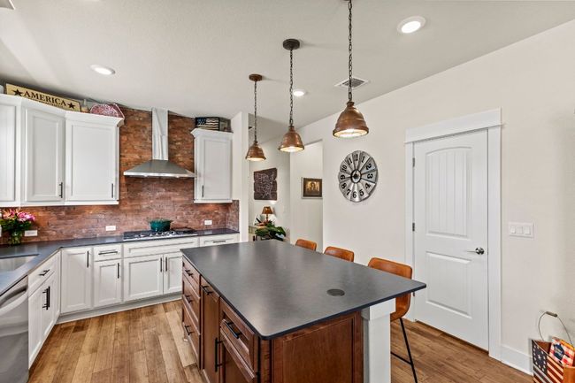 Kitchen featuring stainless steel appliances, dark countertops, visible vents, a kitchen bar, and wall chimney range hood | Image 9