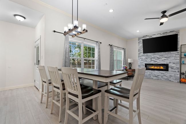 Dining space featuring a fireplace, a chandelier, ornamental molding, light wood-type flooring, and ceiling fan | Image 11