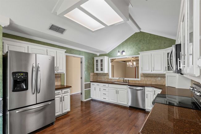 Kitchen with stainless steel appliances, a chandelier, a sink, white cabinets, and vaulted ceiling | Image 8