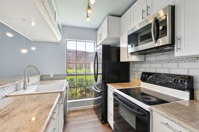 Kitchen with wood-type flooring, electric range, a sink, backsplash, and stainless steel microwave | Image 9