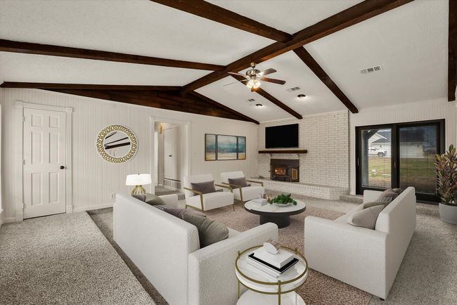 Carpeted living room featuring a fireplace, lofted ceiling with beams, and ceiling fan | Image 5