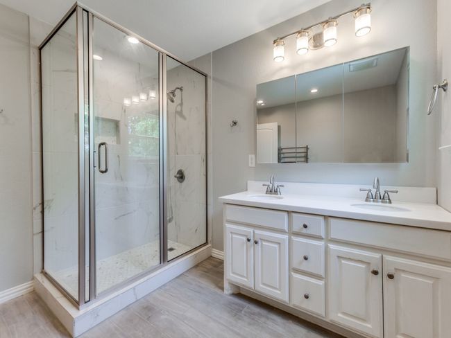 Bathroom featuring a shower stall, double vanity, wood finished floors, and baseboards | Image 15
