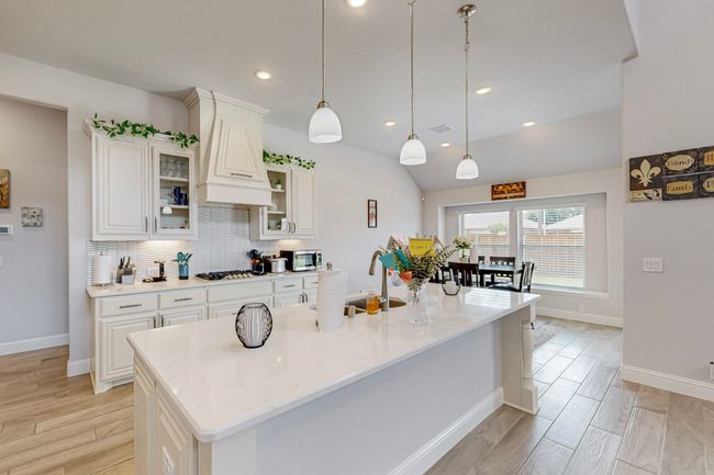 Kitchen featuring tasteful backsplash, wood finish floors, white cabinets, appliances with stainless steel finishes, and glass insert cabinets | Image 7