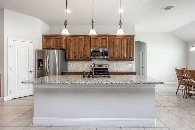 Kitchen with stainless steel appliances, lofted ceiling, arched walkways, decorative backsplash, and light stone counters | Image 13