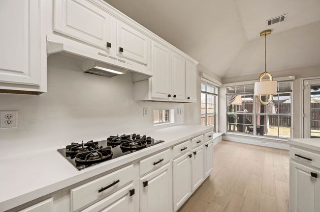 Kitchen featuring light countertops, black gas stovetop, under cabinet range hood, visible vents, and white cabinets | Image 16