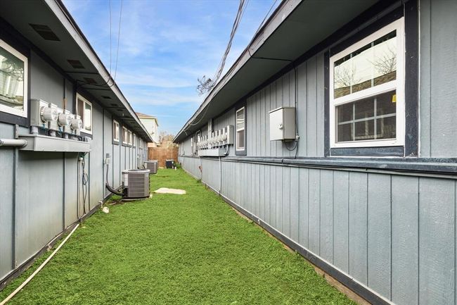 This photo shows a narrow, grassy side yard between the two apartment buildings with windows and separate utility meters for this apartment building. | Image 15