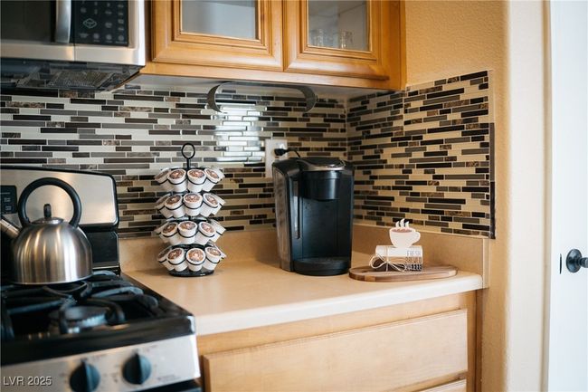 Kitchen view of appliances with stainless steel finishes, light countertops, backsplash, glass insert cabinets, and brown cabinetry | Image 6
