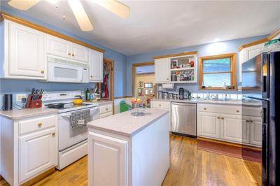 Kitchen featuring white appliances, light hardwood / wood-style floors, a center island, ceiling fan, and white cabinets | Image 2