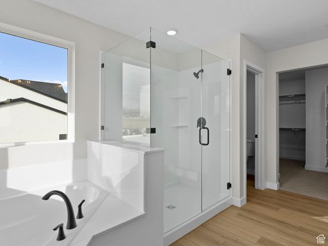 Full bathroom featuring a stall shower, baseboards, wood finished floors, a spacious closet, and a bath | Image 23