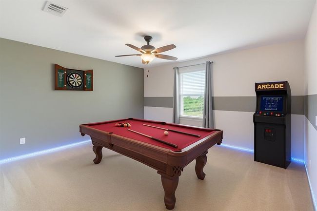 The game room offers a vibrant space to relax or entertain, featuring custom paint, plush carpet, a ceiling fan for comfort, and a window with privacy blinds to control light and ambiance. | Image 13