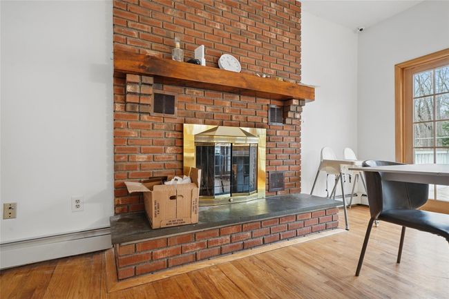 Living area with a baseboard radiator, wood finished floors, visible vents, and a fireplace | Image 10