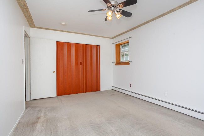 Unfurnished bedroom with carpet, a baseboard radiator, crown molding, a closet, and a ceiling fan | Image 12