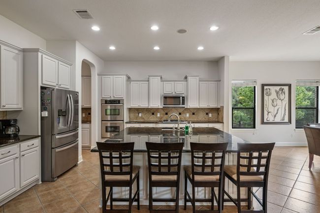 Kitchen with arched walkways, light tile patterned floors, stainless steel appliances, backsplash, and visible vents | Image 9