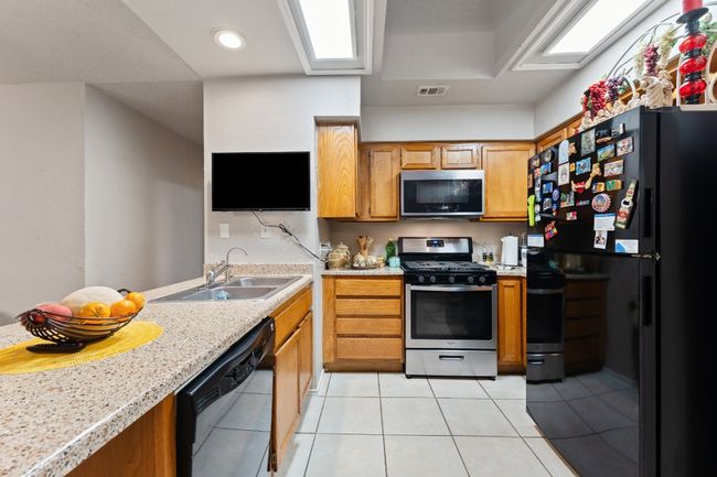 Kitchen featuring black appliances, light tile patterned floors, brown cabinetry, and recessed lighting | Image 8
