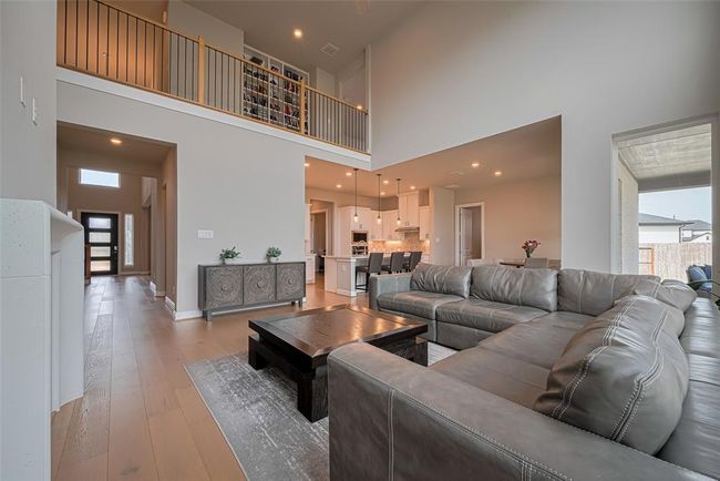 This spacious living area features a high ceiling and an open concept design, connecting seamlessly with the modern kitchen. It includes ample natural light from large windows and an upstairs overlook. | Image 10