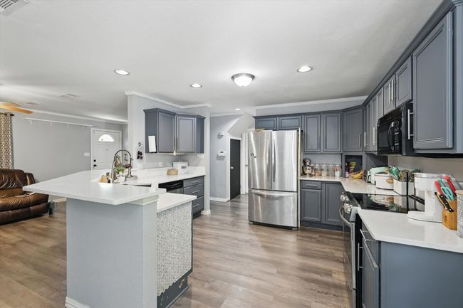 Kitchen featuring appliances with stainless steel finishes, a peninsula, open floor plan, ornamental molding, and wood finished floors | Image 11