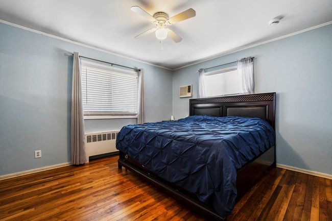 Bedroom featuring radiator heating unit, a wall unit AC, ornamental molding, wood-type flooring, and baseboards | Image 9