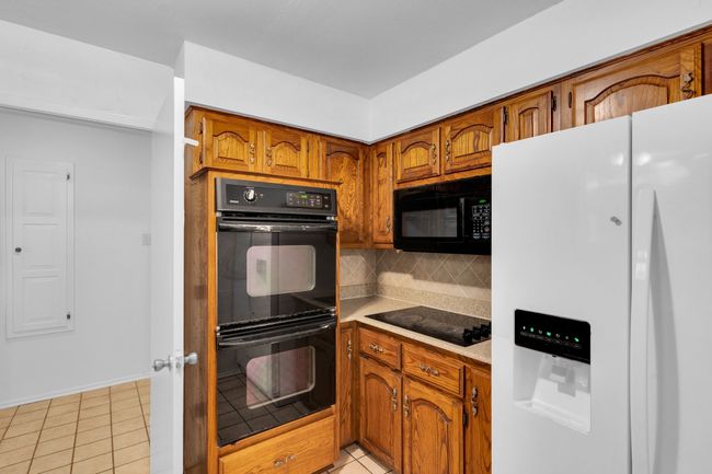 Kitchen featuring brown cabinets, light countertops, light tile patterned floors, backsplash, and black appliances | Image 13