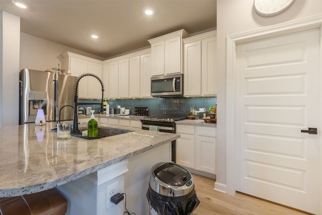Kitchen with stainless steel appliances, white cabinets, light wood-type flooring, light stone countertops, and recessed lighting | Image 11
