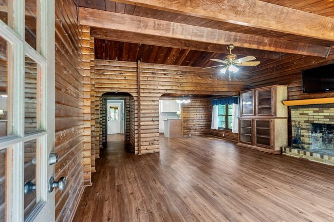 Living room featuring rustic walls, hardwood / wood-style flooring, a brick fireplace, a wood ceiling with exposed beams, and a ceiling fan | Image 4