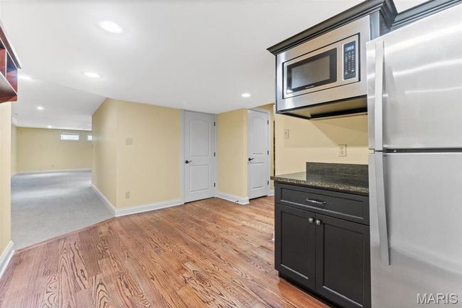 Kitchen with appliances with stainless steel finishes, light wood finished floors, dark countertops, dark cabinetry, and recessed lighting | Image 49
