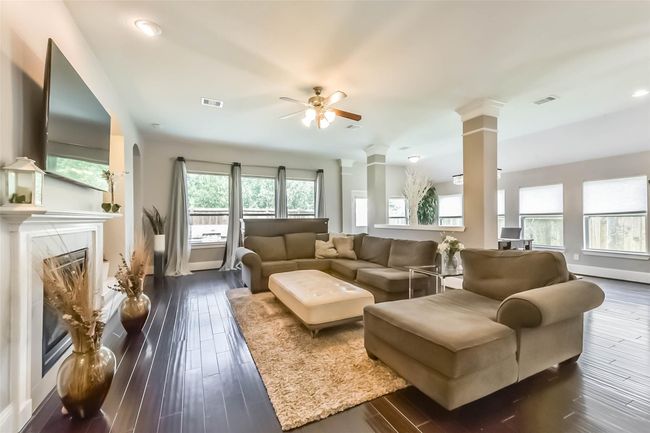 This spacious living room features elegant hardwood floors, a cozy fireplace with built-in shelves, and ample natural light from large windows. The neutral color palette and modern ceiling fan create a welcoming atmosphere. | Image 7