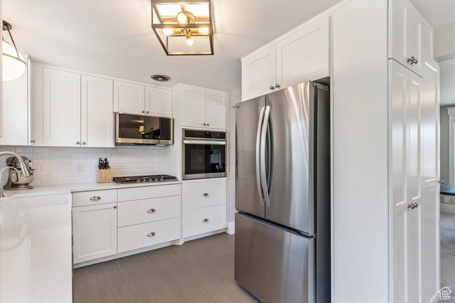 Kitchen with stainless steel appliances, white cabinetry, light countertops, and backsplash | Image 16