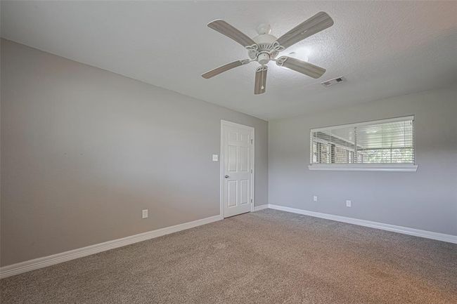 Spacious primary bedroom offers plenty of natural lighting from windows on two walls, a built-in wall storage cabinet, and an en-suite bathroom | Image 14