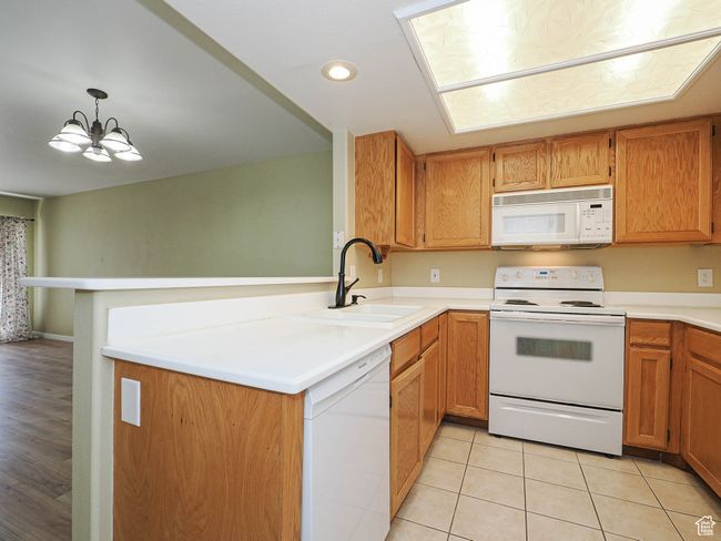 Kitchen featuring a peninsula, a sink, a chandelier, white appliances, and light countertops | Image 10