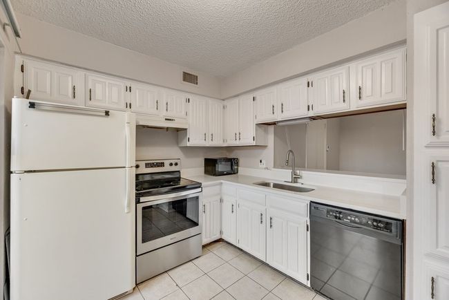 Kitchen with black appliances, light countertops, white cabinetry, light tile patterned floors, and a textured ceiling | Image 8