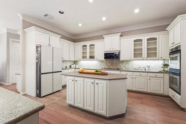 This spacious kitchen features elegant white cabinetry, a large central island, and top of the line appliances. | Image 8