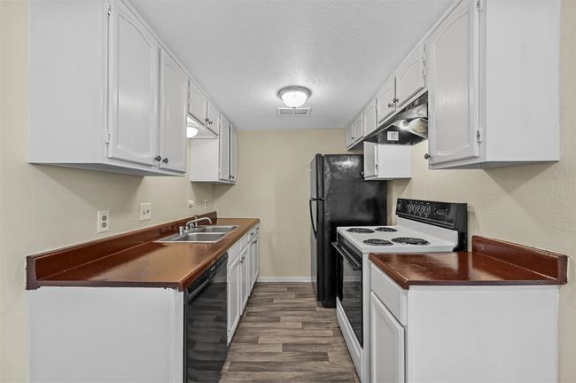 Kitchen with white range with electric cooktop, dishwasher, dark countertops, dark wood-style floors, and under cabinet range hood | Image 4