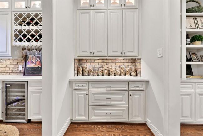Adjacent to the wine room, the butler’s pantry provides seamless flow between the entertainment spaces. With floor-to-ceiling white cabinetry, matching Taj Mahal countertops, and a coordinating brick accent backsplash, this area is both practical and polished—ideal for prep, storage, or an extension of your entertaining layout. | Image 9