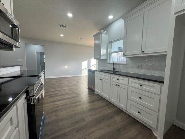 Kitchen featuring stainless steel appliances, dark countertops, dark wood-type flooring, recessed lighting, and backsplash | Image 11