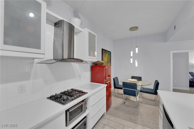 Kitchen featuring stainless steel appliances, wall chimney exhaust hood, white cabinets, and light countertops | Image 15
