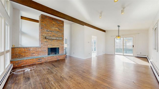 Unfurnished living room with wood finished floors, baseboards, lofted ceiling with beams, a baseboard heating unit, and a brick fireplace | Image 4