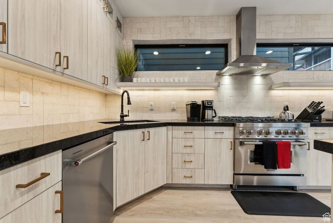 Kitchen with backsplash, range hood, light hardwood / wood-style floors, sink, and appliances with stainless steel finishes | Image 9