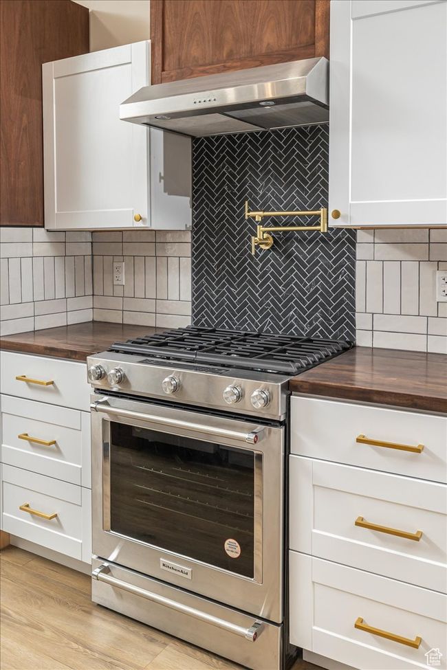 Kitchen featuring tasteful backsplash, stainless steel range, white cabinets, and ventilation hood | Image 14