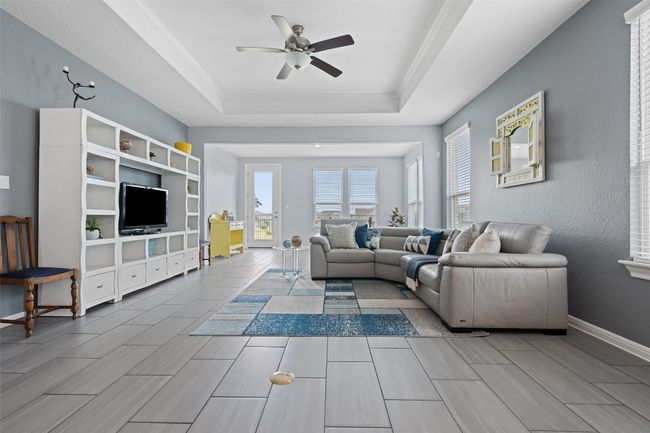 Living area featuring a raised ceiling, ceiling fan, crown molding, tile floors, and large windows. | Image 8