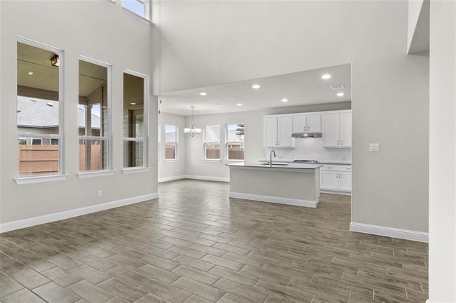 Unfurnished living room with a sink, a chandelier, wood finish floors, baseboards, and a high ceiling | Image 7