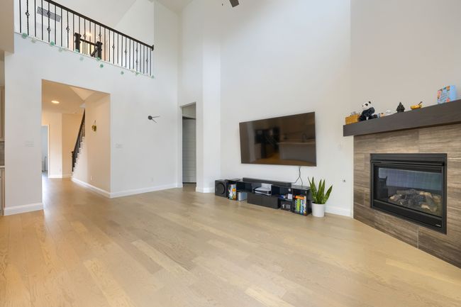 Living room with a ceiling fan, stairs, wood finished floors, a tile fireplace, and baseboards | Image 8