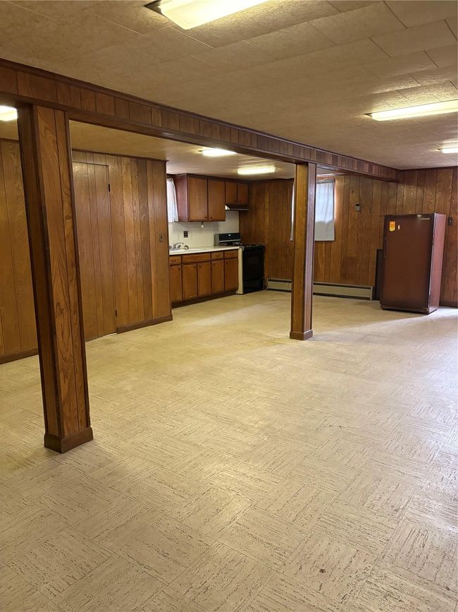 Finished below grade area with wooden walls, a baseboard heating unit, light floors, and refrigerator | Image 15