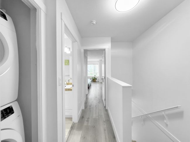 Hall with light wood-type flooring, an upstairs landing, stacked washer and dryer, and baseboards | Image 17